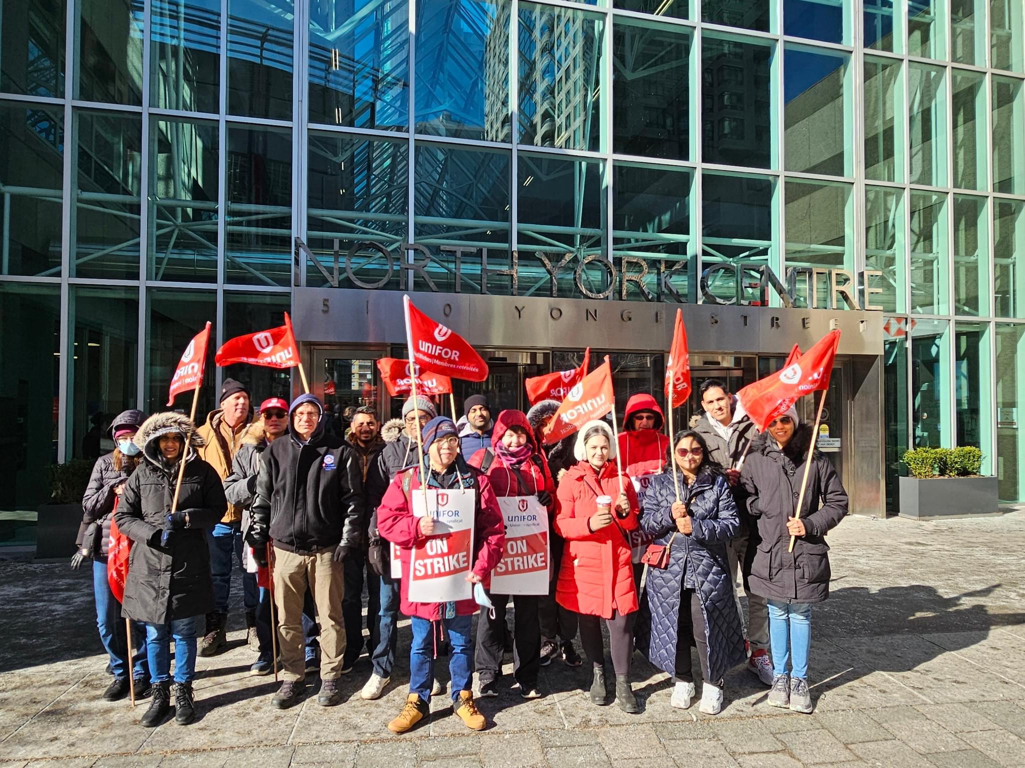 A group of people standing outside an office tower with red Unifor flags.