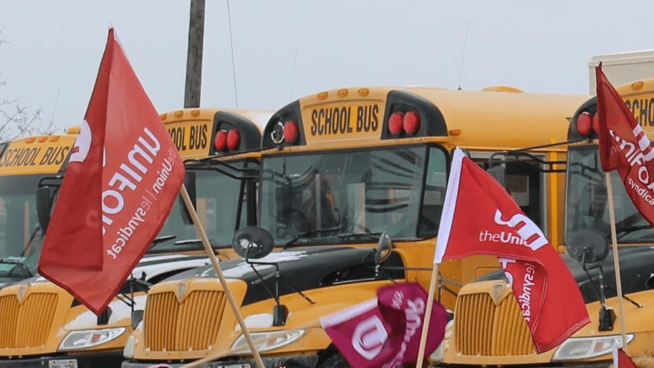 Yellow school buses with red Unifor flags in the foreground.